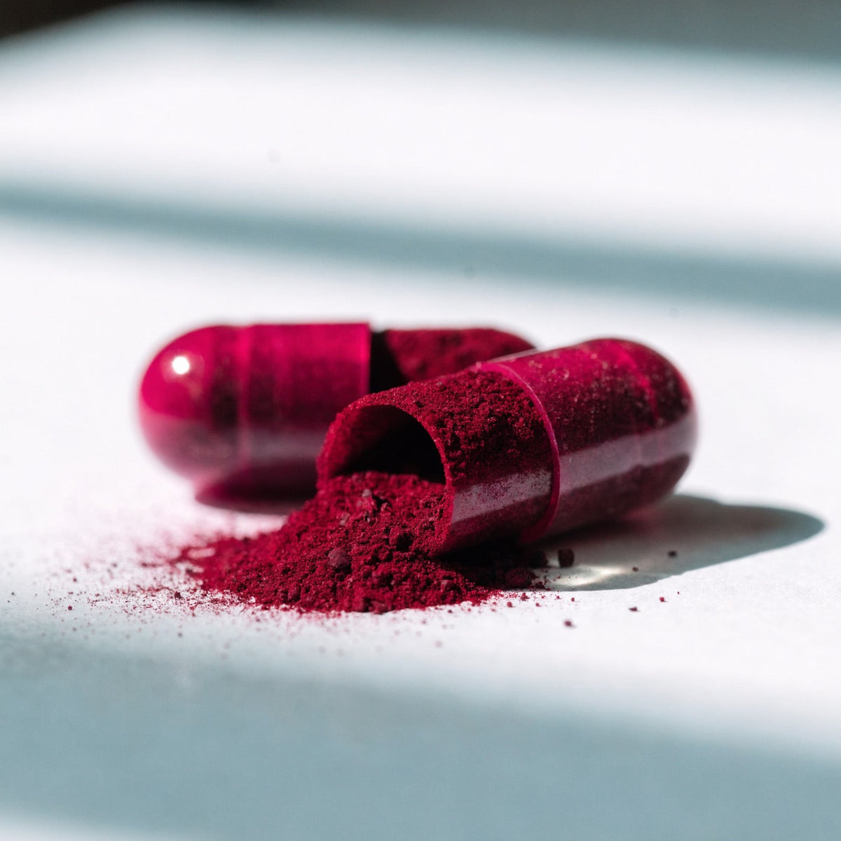 Close-up of two capsules, one opened to show the beetroot powder.